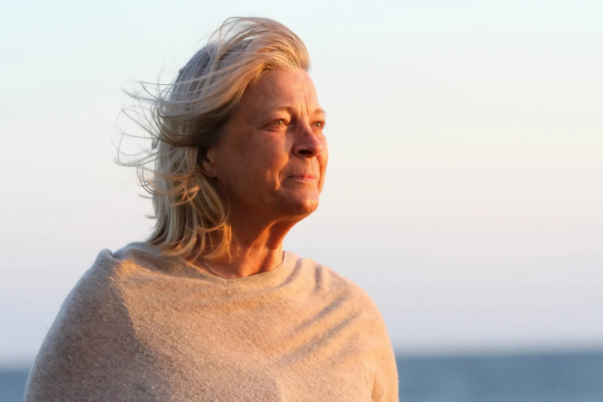 A woman with wind-swept hair looking out over the water in golden evening light